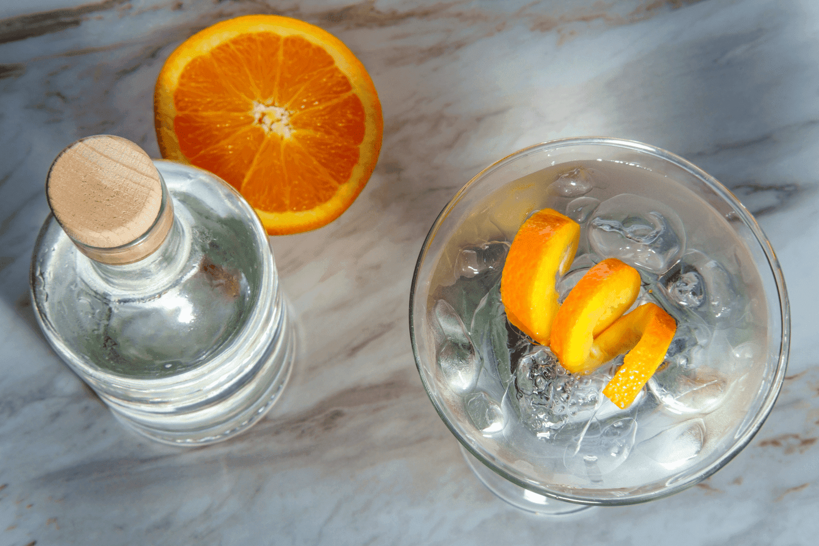 Overhead view of a gin martini with orange peel garnish, beside a bottle and orange slice