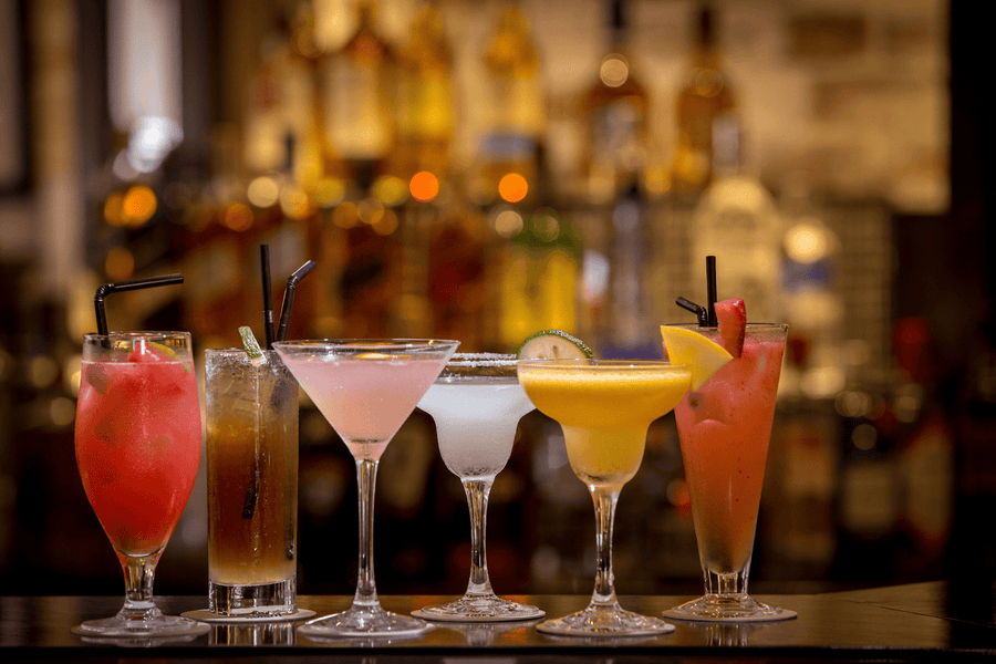 Assorted colorful cocktails lined up on a bar counter.