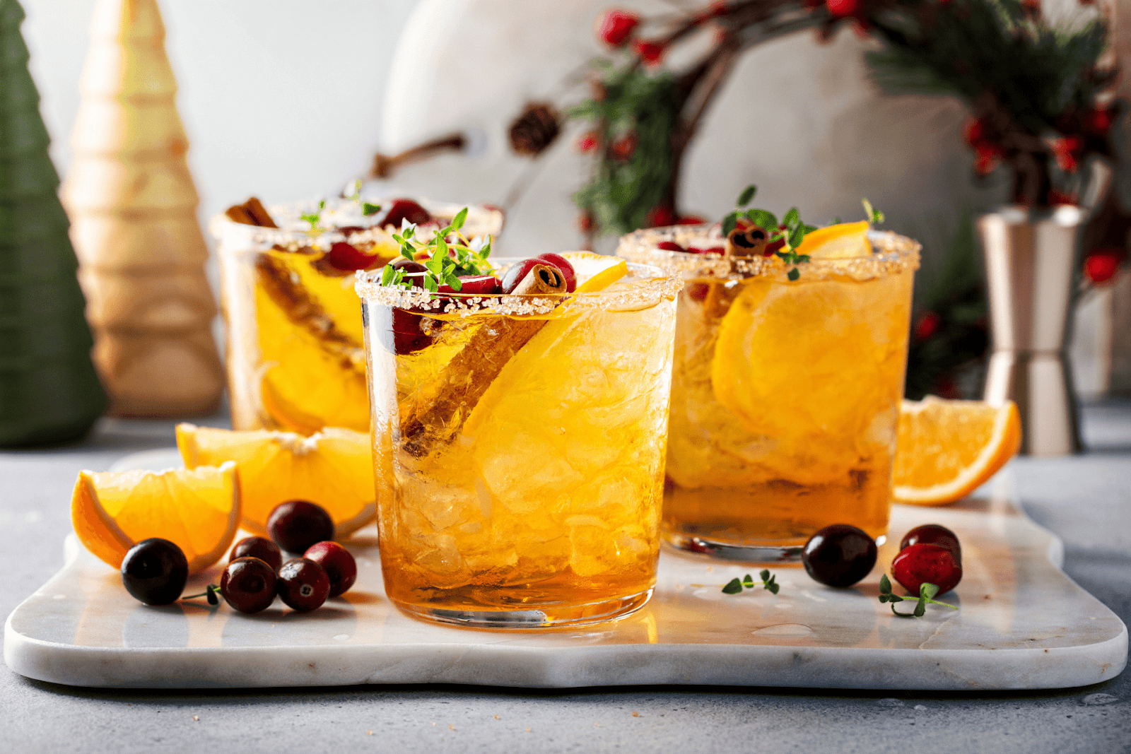 Christmas cocktail with ice, spicy garnish, and half an orange beside it.
