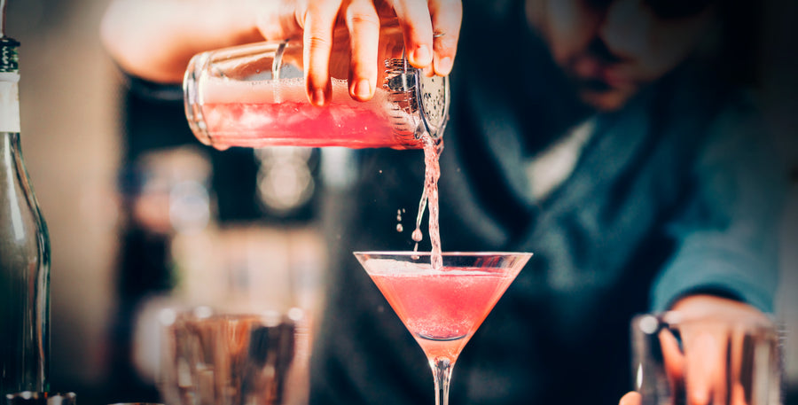 a bartender pouring a cosmopolitan cocktail into a martini glass