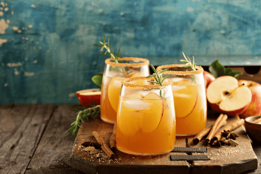 Fall apple cocktails with cinnamon sticks and rosemary garnish on a rustic table.