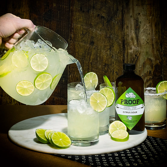 a football party host pours big batch Proof Syrup margaritas from a pitcher