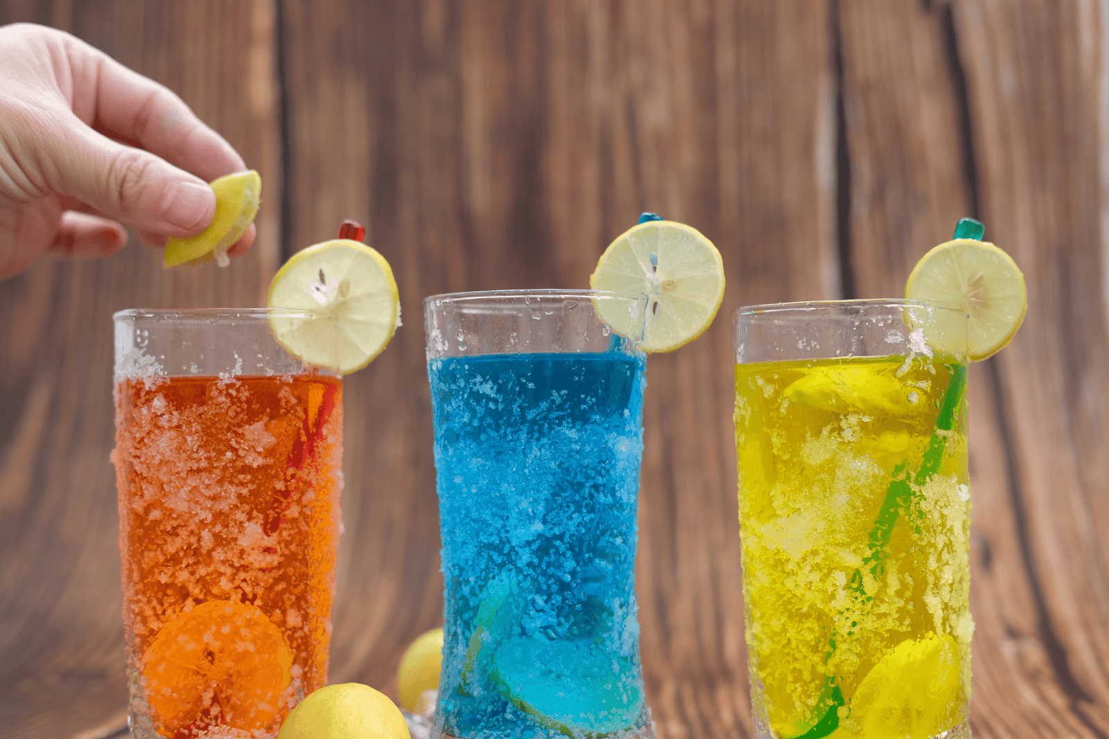 Three colorful drinks with lemon slices on a wooden background.