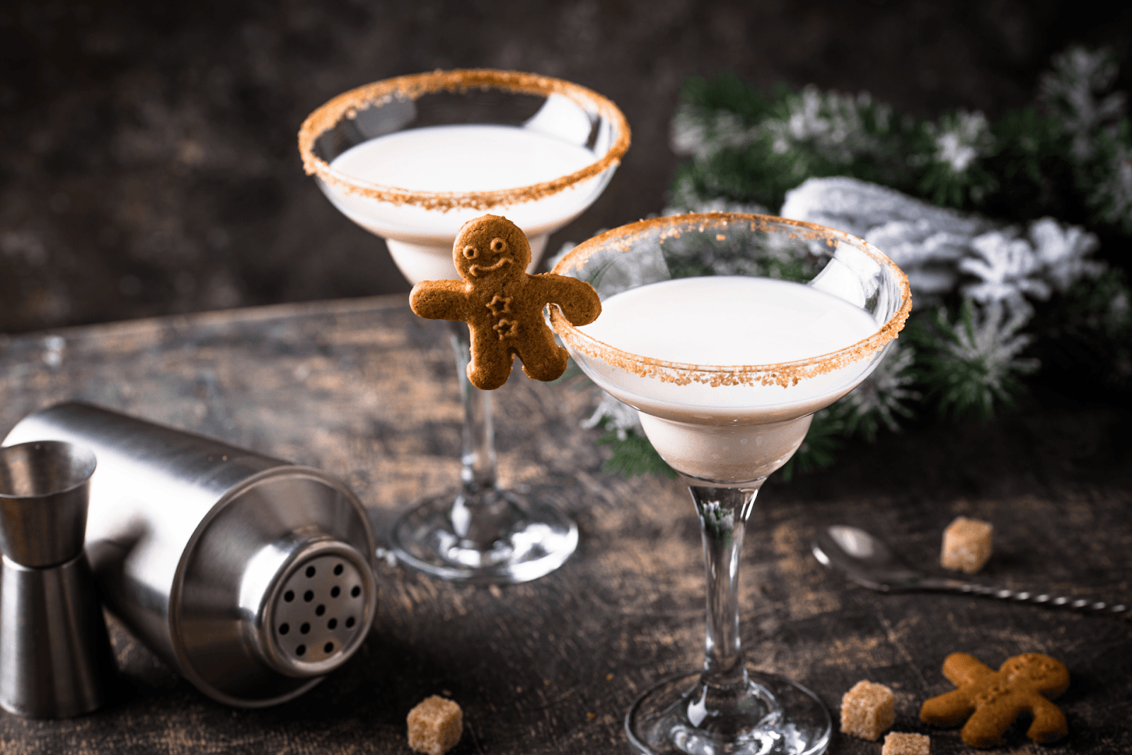 Two creamy holiday cocktails in sugar-rimmed glasses, garnished with a small gingerbread cookie.