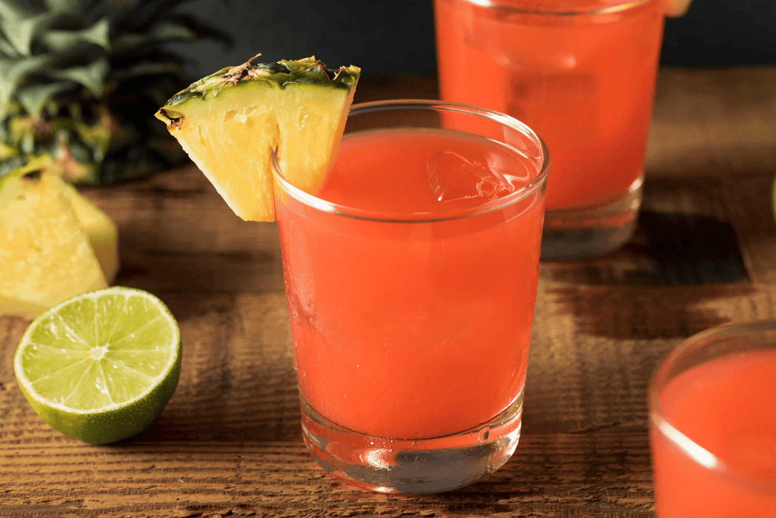 Rum punch cocktail in a short glass with ice, garnished with a pineapple wedge and lime.