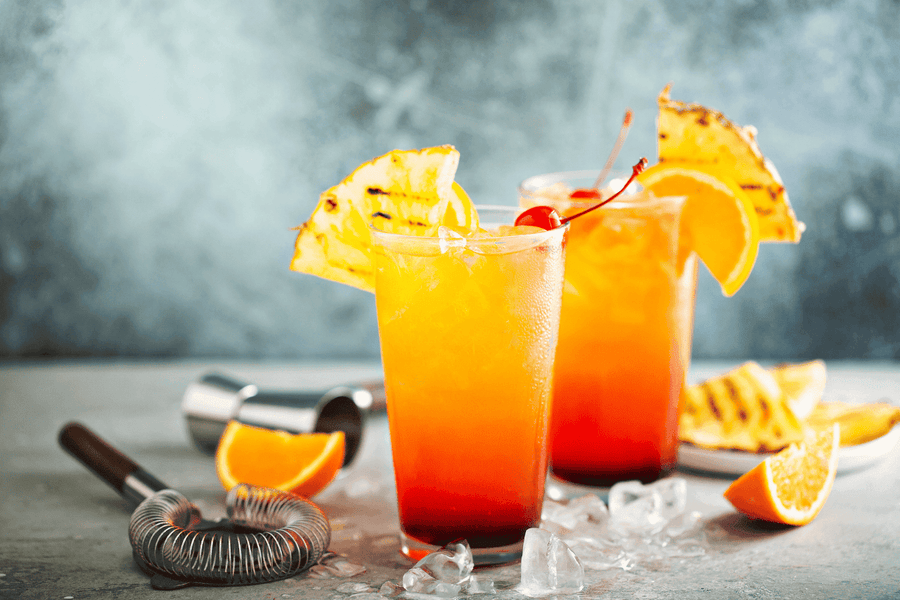 Two Tequila Sunrise cocktails garnished with pineapple, orange, and cherries