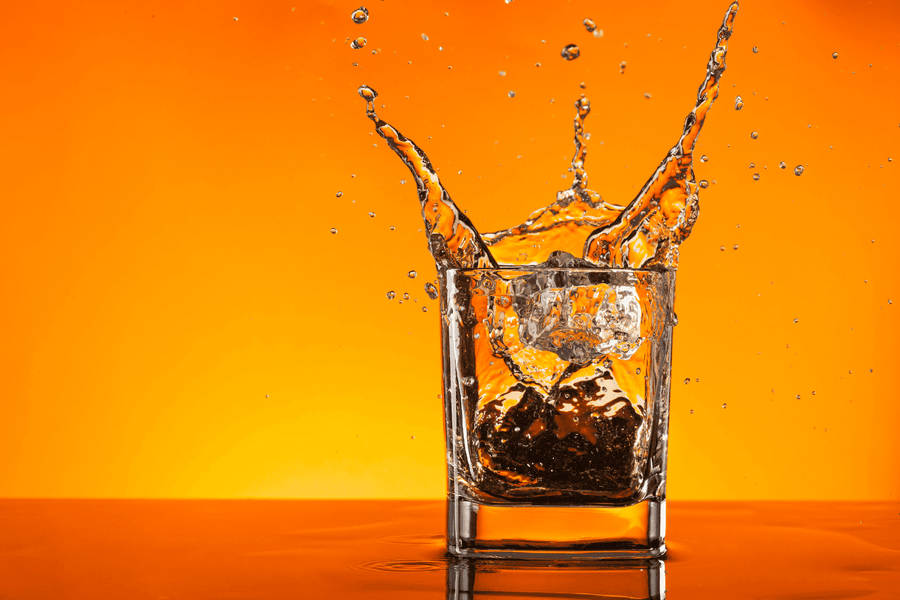 Ice cubes splashing into a glass of whiskey with an orange background.