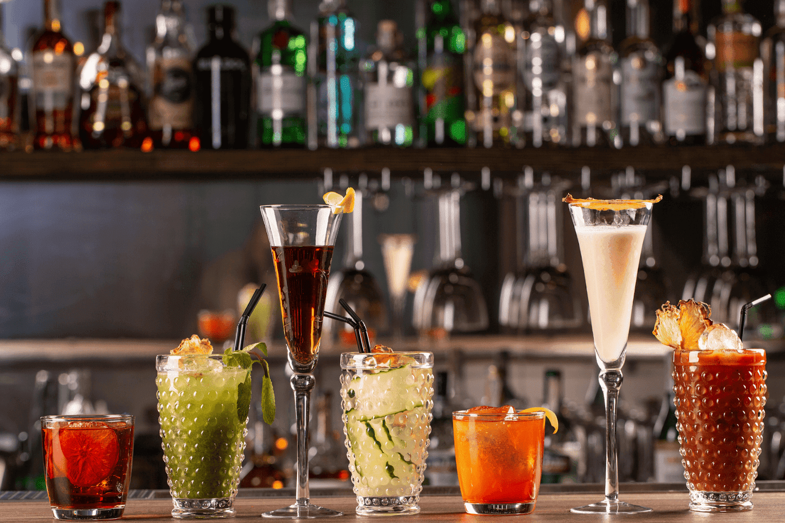Assortment of vibrant cocktails lined up on a bar counter with bottles in the background