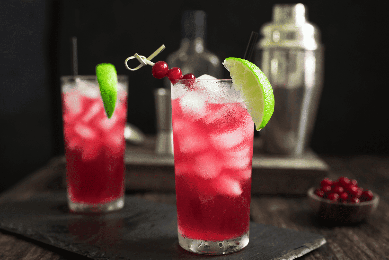 Vodka Cranberry cocktail with ice, lime wedge, and berries garnish in a tall glass