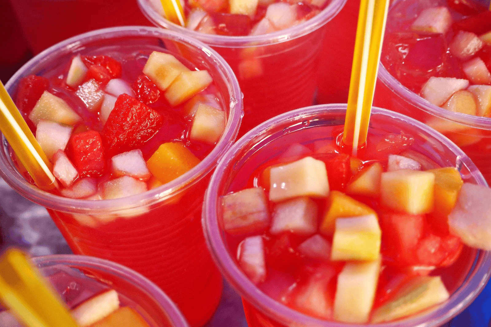 Cups of bright red jungle juice with diced fruit and yellow straws