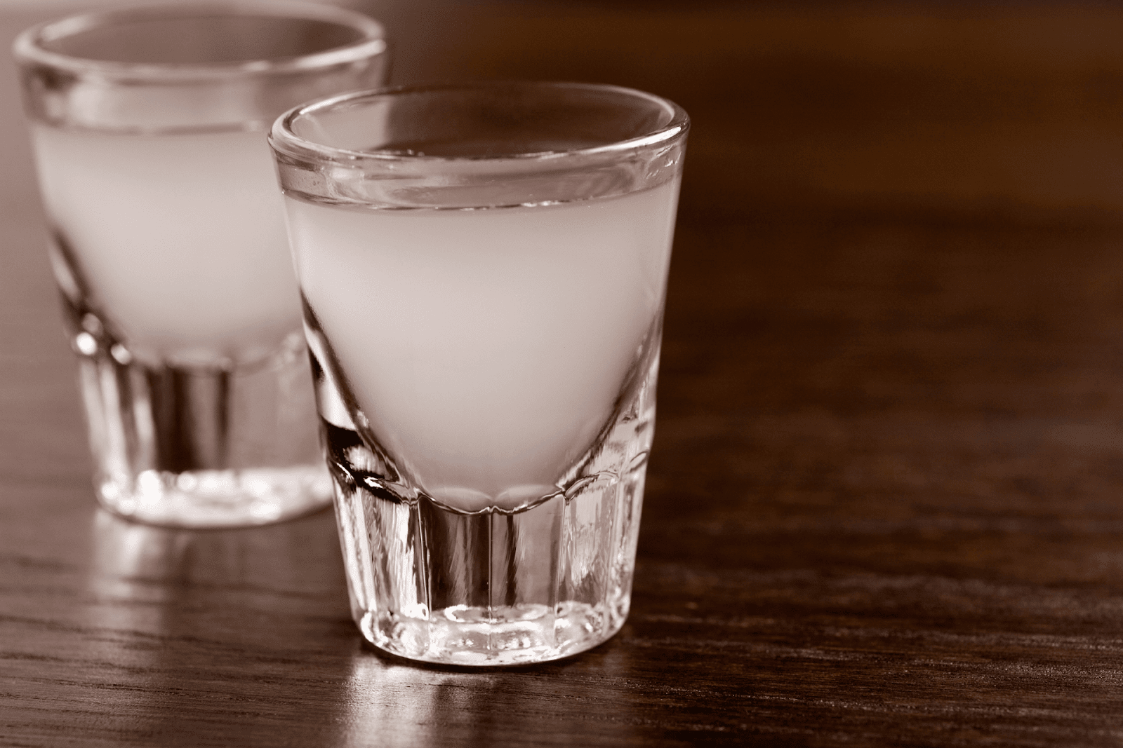 Two chilled lemon drop shots on a wooden bar surface.