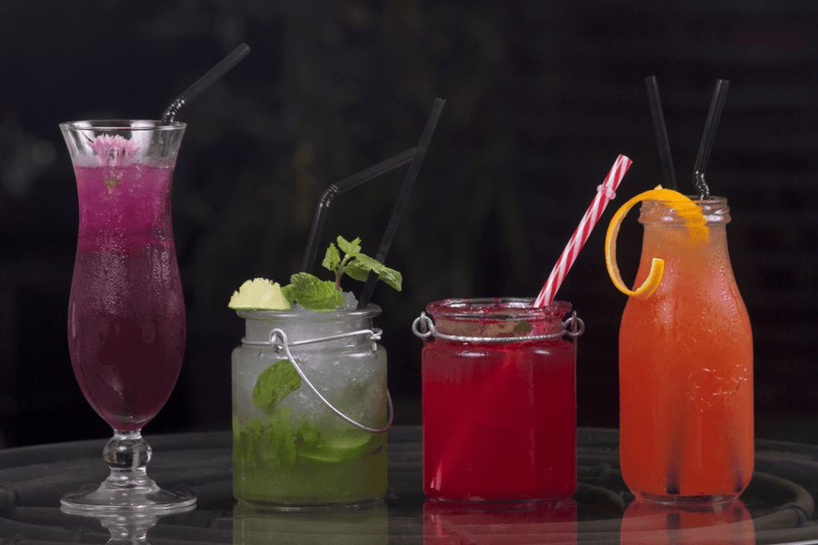 Four colorful mocktails in different glasses with straws, garnished with fruit and mint.