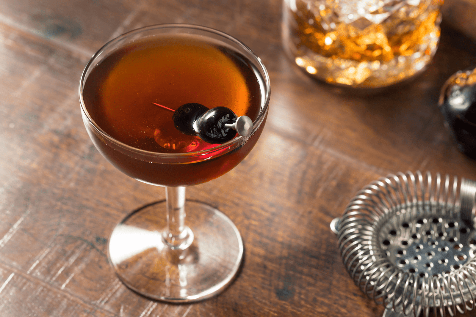 Classic Manhattan cocktail garnished with cherries on a wooden bar surface.
