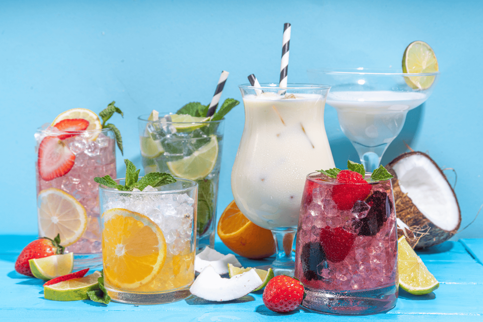 Colorful assortment of fruity mocktails with ice, citrus, and berries against a blue background