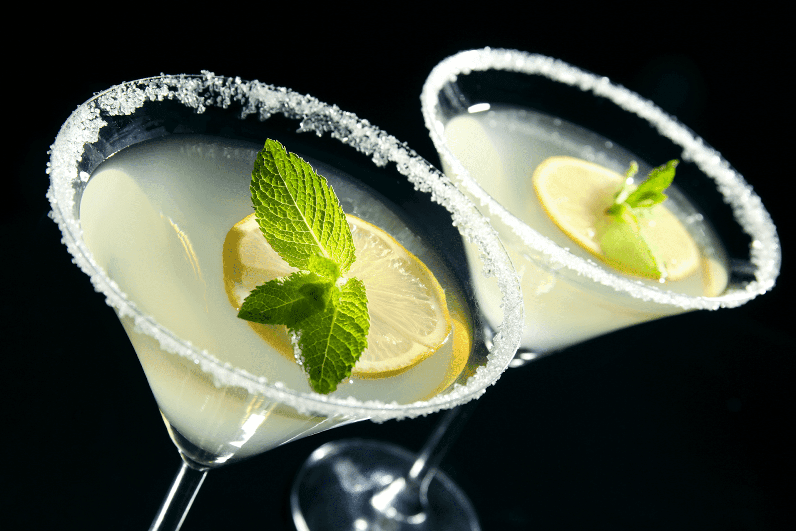 Two Lemon Drop cocktails in martini glasses with sugared rims, garnished with lemon slices and fresh mint
