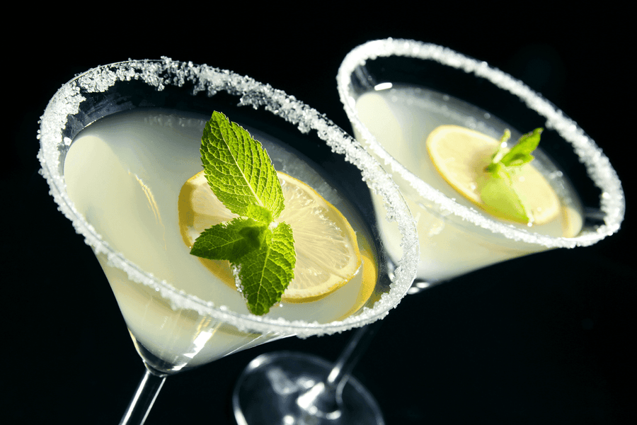 Two Lemon Drop cocktails in martini glasses with sugared rims, garnished with lemon slices and fresh mint