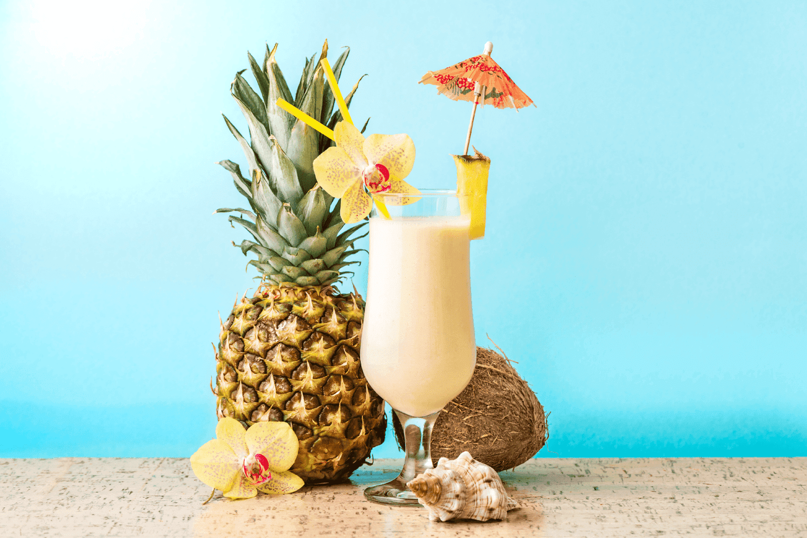 Tropical pina colada with pineapple, coconut, and a cocktail umbrella on a blue background.