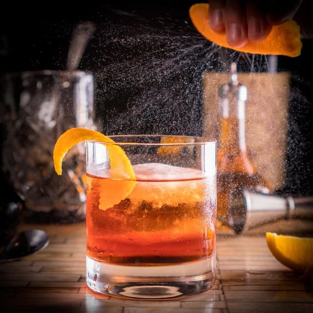 Cocktail with a squeeze of orange on top of a bar, featuring bar utensils