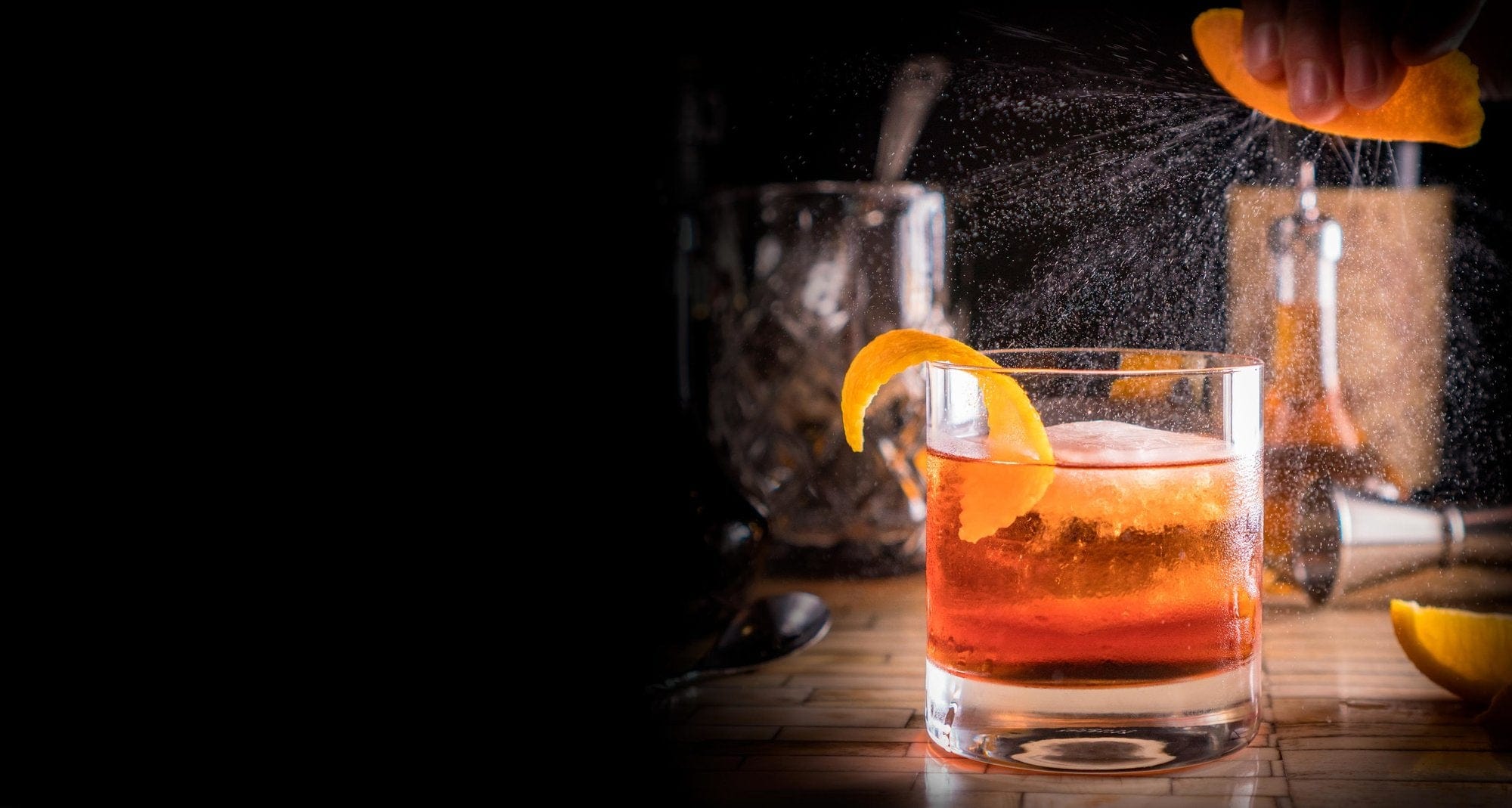 Cocktail with a squeeze of orange on top of a bar, featuring bar utensils